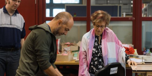 Ein Mann in olivfarbenen Pullover zeigt zwei Kollegen einen Arbeitsschritt in der Druckerei.