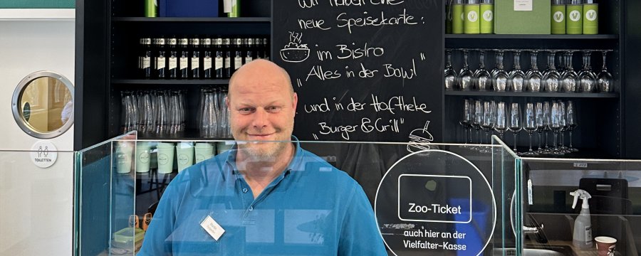 Mann in blauem Poloshirt steht hinterm Tresen im Bistro.