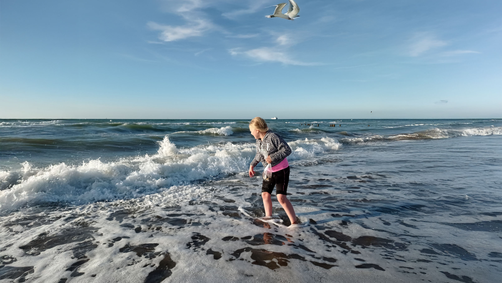 Ein Kind am Strand steht mit dem Füßen in den Wellen.