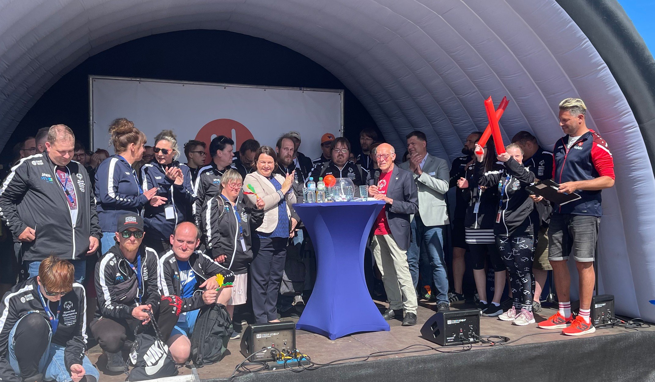Eine Gruppe Sportler steht hinter einem Stehtisch auf einer Bühne.