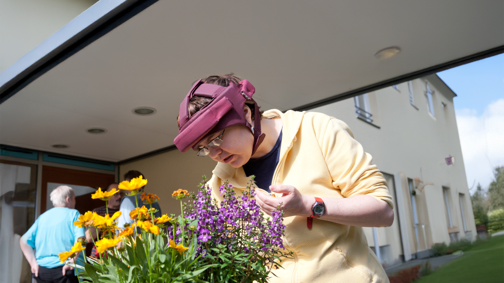 Ein Frau betrachtet bunte Blumen vor einem Hauseingang.