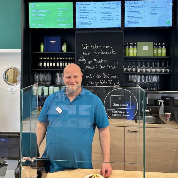 Mann in blauem Poloshirt steht hinterm Tresen im Bistro.