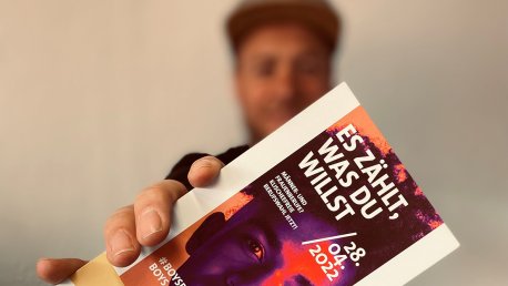 Ein Mann hält einen Flyer in die Kamera.
