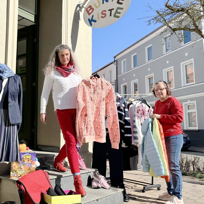 Zwei Frauen hängen Kleidung vor einem Laden auf.