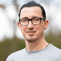 Nahaufnahme eines Mannes mit schwarzen zurückgekämmten Haaren und einer Brille