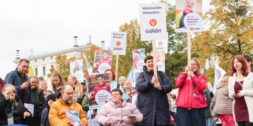 Eine Menschengruppe, zum Teil Rollstuhlfahrer, demonstrieren mit Schildern und Plakaten