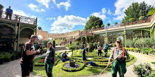 Männer und Frauen pflegen den sommerlichen Garten hinter dem Schweriner Schloss