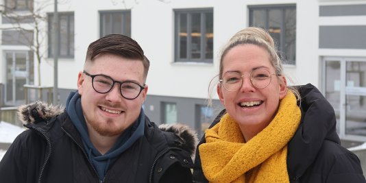 Ein Mann und eine Frau stehen im Winter lächelnd vor einem Neubau.