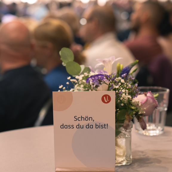 Tischschild steht in einem Saal vor einem kleinen Blumenstrauß