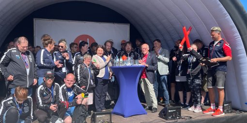 Eine Gruppe Sportler steht hinter einem Stehtisch auf einer Bühne.