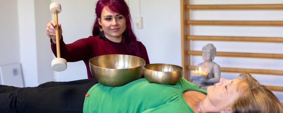 Eine junge Frau führt eine Klangschalentherapie an einer Patientin durch.