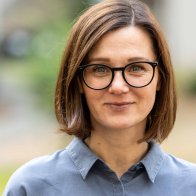 Nahaufnahme einer Frau mit brünettem Haar und dunkler Brille vor unscharfen Hintergrund