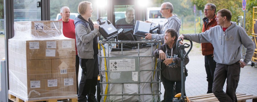 Eine Gruppe von Männern steht an einem Gabelstapler und lädt Elektroschrott in eine Box