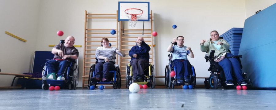 Fünf Rollstuhlfahrer trainieren in der Turnhalle das Boccia-Spiel.