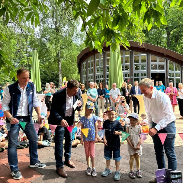 Erwachsene und Kinder durchschneiden eine Wimpelkette und eröffnen so den barrierefreien Spielplatz im Schweriner Zoo.