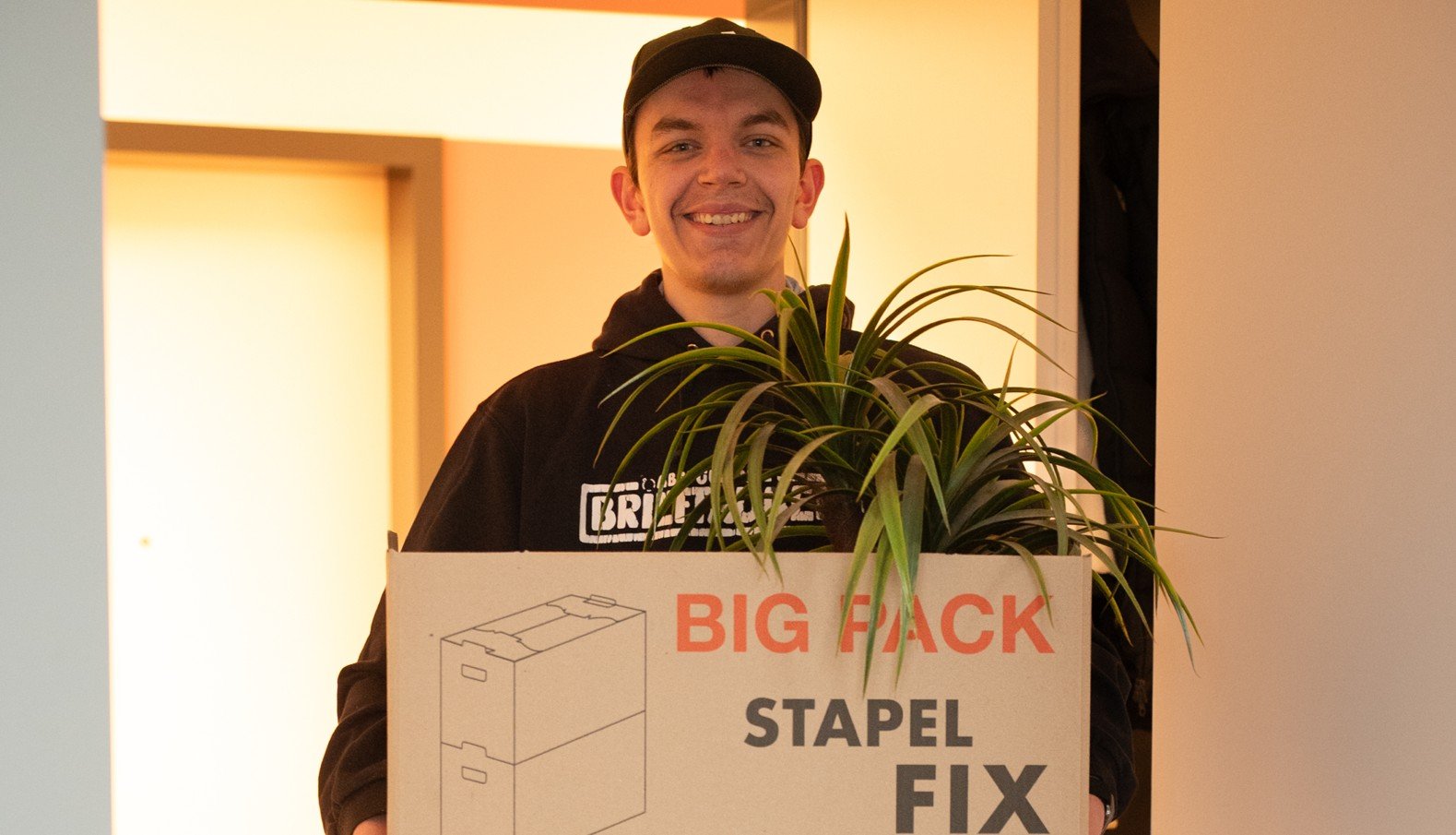Ein junger Mann mit Basecap trägt einen Umzugskarton