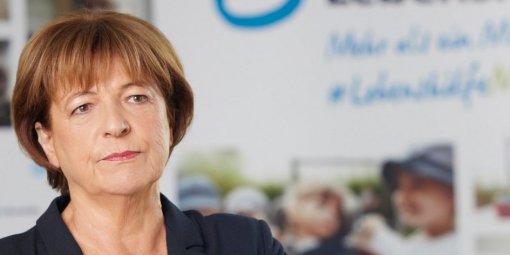 Eine Frau im Blazer steht vor einem Schild der Lebenshilfe