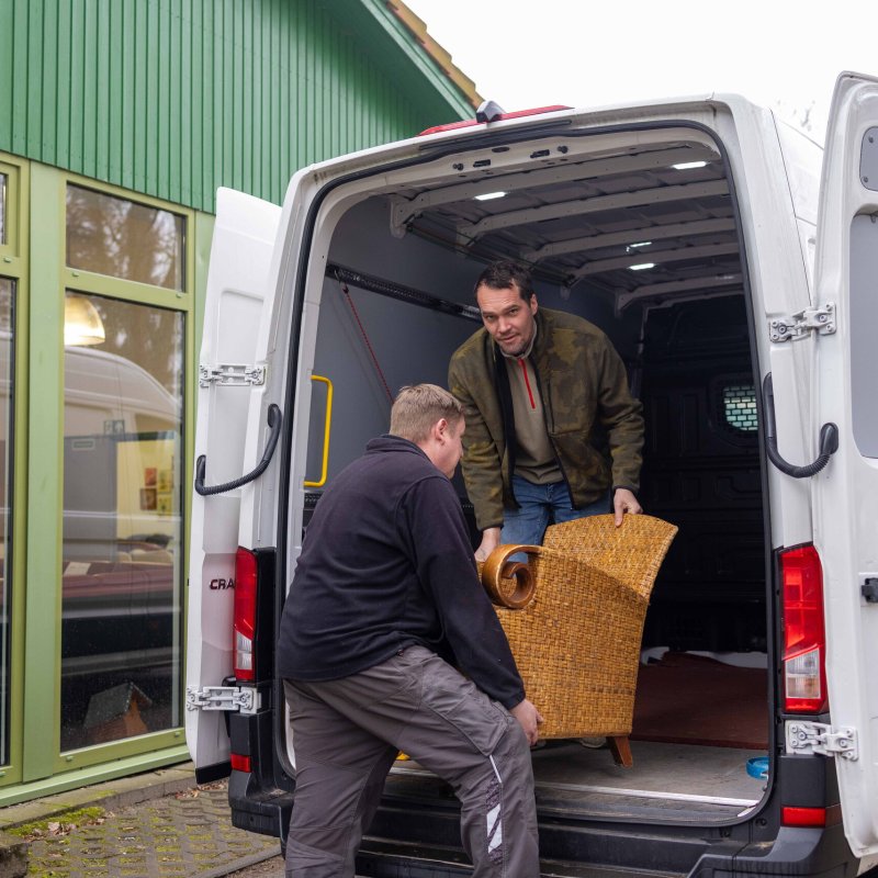 Zwei Männer laden Möbel aus einem Transporter aus.