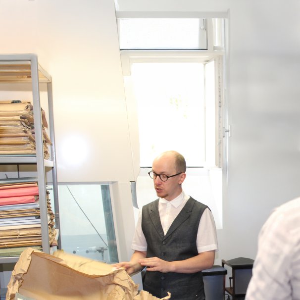 Ein Mann mit Brille, Hemd und Weste holt Unterlagen aus einem Archivregal