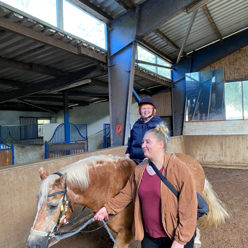 Ein Kind reitet in einer Halle auf einem Pferd das von einer Frau geführt wird