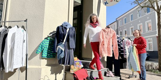 Zwei Frauen hängen Kleidung vor einem Laden auf.