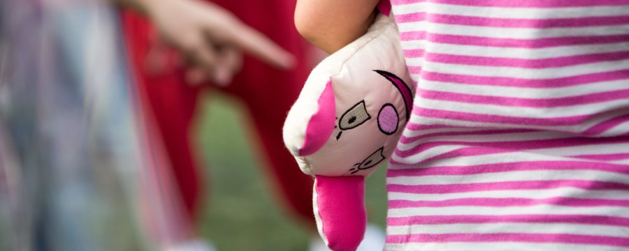 Ein Mensch in gestreiftem T-Shirt hat sich ein Kuscheltier unter den Arm geklemmt.