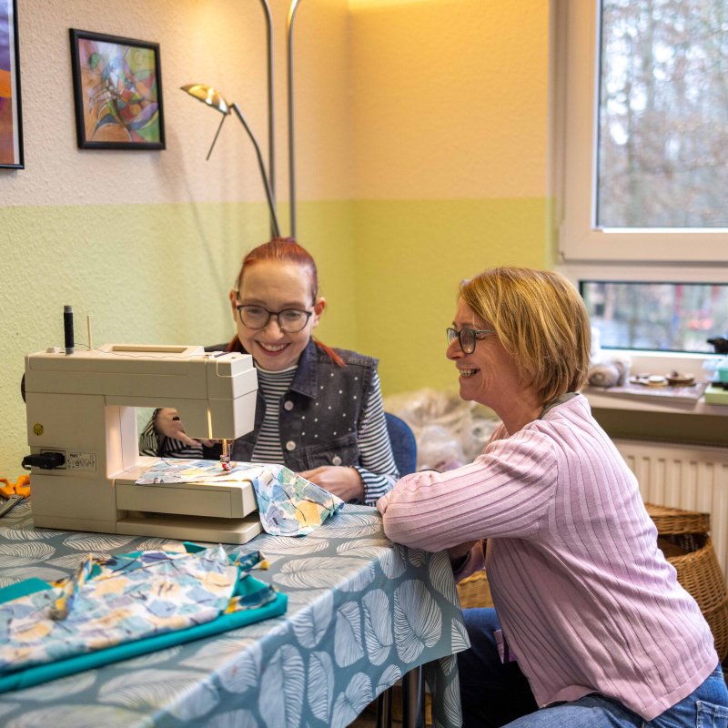 Zwei Frauen sitzen lächelnd an eine Nähmaschine