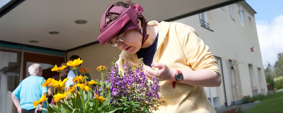 Ein Frau betrachtet bunte Blumen vor einem Hauseingang.