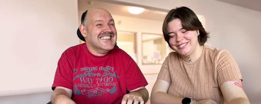 Eine junge Frau und ein Rollstuhlfahrer sitzen am Tisch und puzzeln.