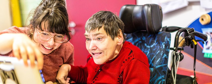 Eine Kollegin aus dem Team Unterstützende Kommunikation erklärt einem Menschen mit Unterstützungsbedarf das Hilfsmittel.