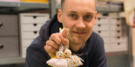 Ein junger Mann zeigt lächelnd kleine Hasen aus Stoff