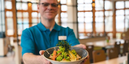 Ein Mitarbeiter aus dem Bistro zeigt eine Bowl mit Gemüse.