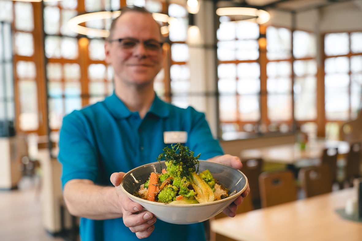 Ein Mitarbeiter aus dem Bistro zeigt eine Bowl mit Gemüse.