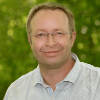 Nahaufnahme eines Mannes mit randloser Brille vor grünem unscharfen Hintergrund