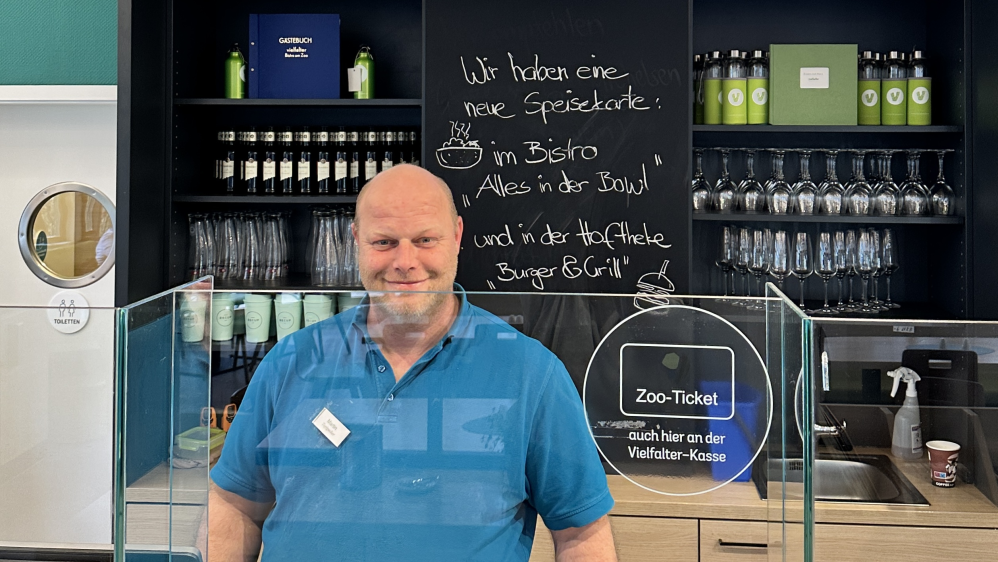 Mann in blauem Poloshirt steht hinterm Tresen im Bistro.