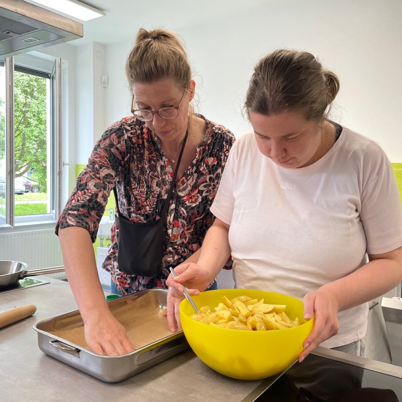 Zwei Frauen bereiten ein Ofenblech mit Kartoffelspalten vor