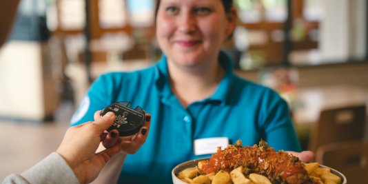 Eine Mitarbeiterin des Bistro reicht das bestellte Essen und nimmt dafür den Summer zurück.