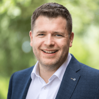 Nahaufnahme eines lächelnden Mannes vor grünem unscharfen Hintergrund