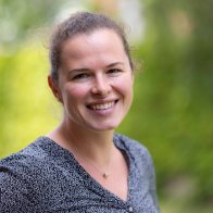 Nahaufnahme einer Frau mit dunklen zusammengebundenen Haaren vor grünen unscharfen Haaren
