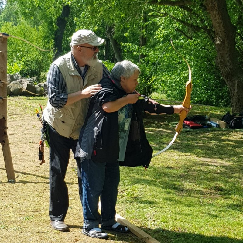 Ein Mann unterstützt eine ältere Frau beim Bogenschießen