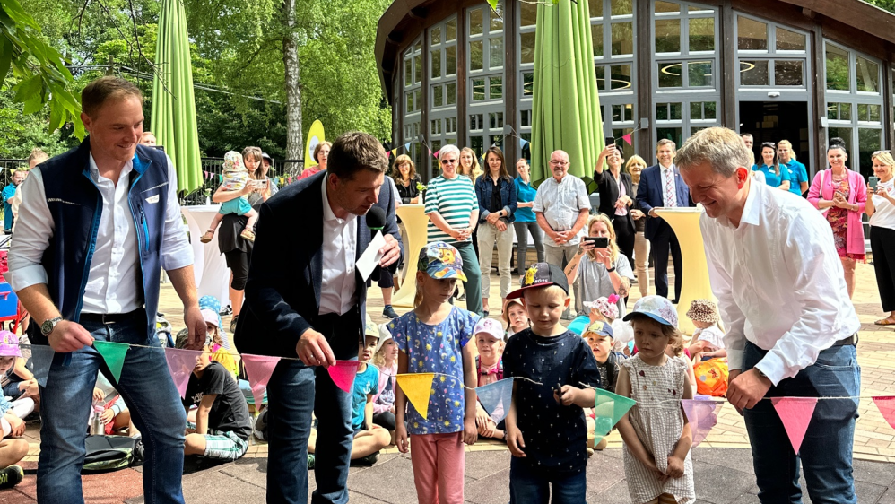 Erwachsene und Kinder durchschneiden eine Wimpelkette und eröffnen so den barrierefreien Spielplatz im Schweriner Zoo.