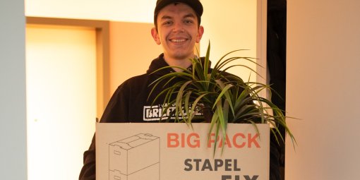 Ein junger Mann mit Basecap trägt einen Umzugskarton