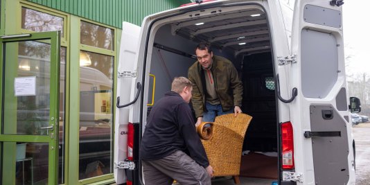 Zwei Männer laden Möbel aus einem Transporter aus.